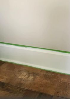 a white toilet sitting on top of a wooden floor next to a bath tub with green trim