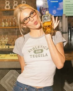 a woman holding up a bottle of beer in her right hand and looking at the camera