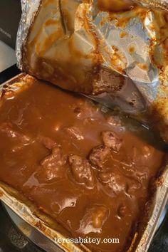 an open tin foil container filled with meat covered in sauce and gravy on top of a stove