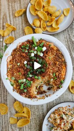 two plates filled with food on top of a wooden table next to chips and dip