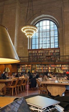 the library is full of books and people are sitting at their desks in front of large windows