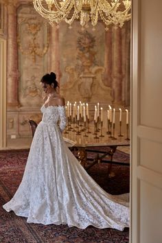 a woman in a wedding dress is standing by a chandelier