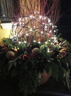 a potted plant with christmas lights and greenery on the top, in front of a window