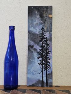 a blue bottle sitting on top of a table next to a painting with trees in it