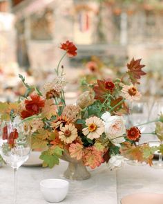 an arrangement of flowers in a vase sitting on a table with wine glasses and plates