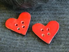 two red heart shaped buttons sitting next to each other on a gray surface with holes in the middle