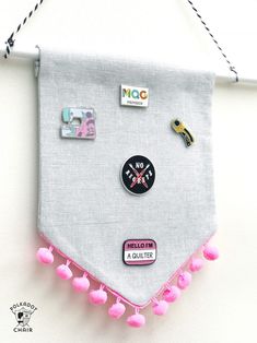 a white wall hanging with pink pom - poms and magnets on it