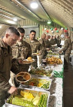 soldiers are serving themselves food from trays on a long table in an indoor area