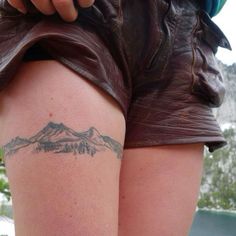 a woman with a tattoo on her thigh showing the mountain range behind her back leg