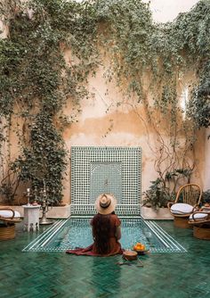 a woman sitting on the ground in front of a pool surrounded by ivy covered walls