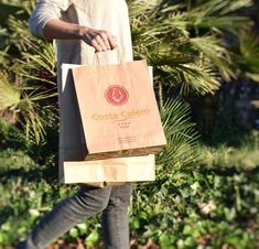 a person carrying a brown paper bag in their hand while walking through the grass and palm trees