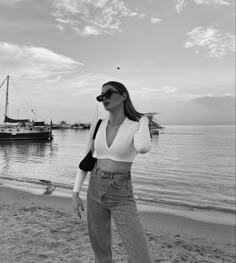 black and white photograph of woman on beach with boats in the background, wearing wide legged jeans