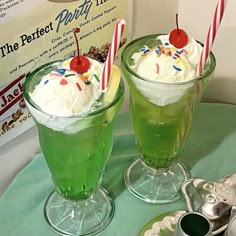 two glasses filled with green liquid and topped with whipped cream, cherries and sprinkles