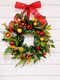 a christmas wreath with oranges, apples and greenery on a white wooden background