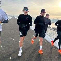 three men running in the snow wearing black and orange shoes