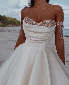 a woman in a white wedding dress on the beach with her hands behind her back