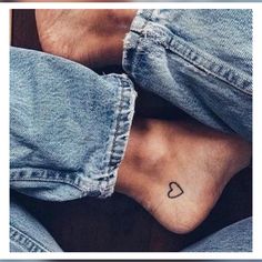 someone has their foot tattooed with a heart on the bottom of their leg and is wearing jeans