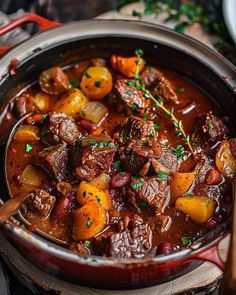 a pot filled with beef and potatoes on top of a wooden table next to a spoon