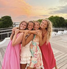 three girls hugging each other while standing on a wooden deck