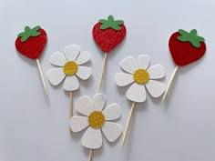 four strawberries and two daisies on sticks