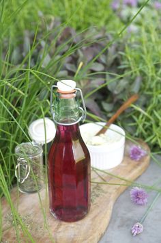 a glass bottle filled with liquid sitting on top of a wooden board next to flowers