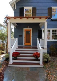 a blue house with white railings and red flowers on the front steps in front of it