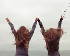 two women standing on the beach with their arms in the air and birds flying overhead