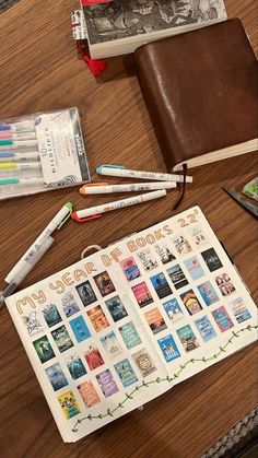 an open notebook sitting on top of a wooden table next to pens and pencils