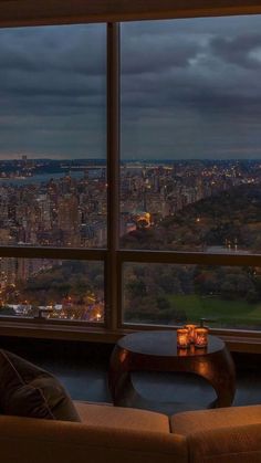 a living room filled with furniture and a large window overlooking a city at night time