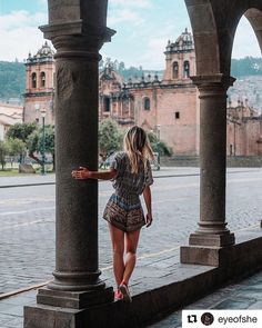 a woman standing on the side of a building next to columns and looking at buildings