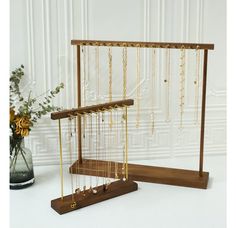 a wooden stand with gold necklaces hanging from it's sides and a vase full of flowers in the background