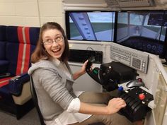 a woman sitting in front of two monitors on top of a desk with a steering wheel