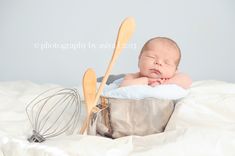 a baby is laying in a metal bowl with whisk and wooden spoons