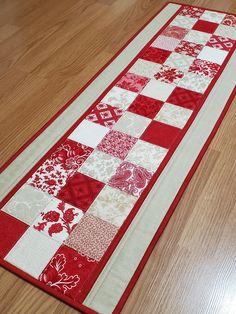 a red and white quilted runner on the floor with wood floors in the background