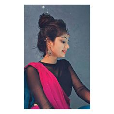 a woman in a black top and pink sari sitting on a chair with her hand on her hip