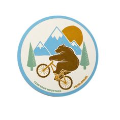 a sticker with a bear riding a bike in front of mountains and pine trees