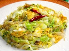 a white plate topped with cabbage and other food on top of a wooden table next to a red pepper