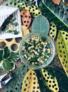 a glass bowl filled with green and yellow seeds next to some leaves on top of a table