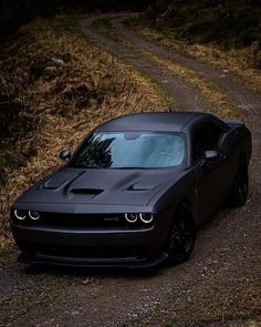 a black car parked on the side of a road next to a dirt road and grass