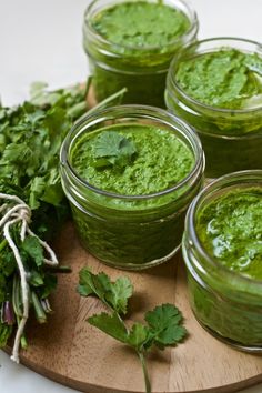 four jars filled with green pesto sitting on top of a wooden cutting board next to parsley