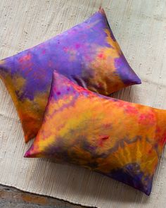 two colorful pillows sitting on top of a white rug next to an orange and purple pillow