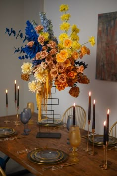 a wooden table topped with a vase filled with flowers next to candles and plates on top of it