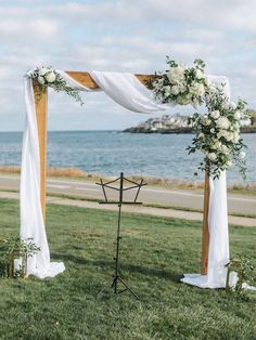 an outdoor ceremony setup with white flowers and greenery on the grass near the water