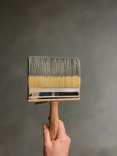 a hand holding a paint brush with a white bristles on the top and yellow bristles on the bottom