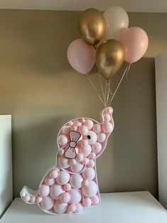 a pink and gold elephant with balloons floating from it's back on a shelf