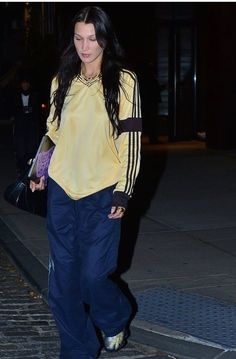 a woman walking down the street at night with her hand in her pocket and wearing adidas sneakers