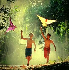 two young boys are running in the woods with kites above their heads and one boy is holding his hand up