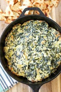 spinach and cheese pizza in a cast iron skillet on a wooden table with pita chips