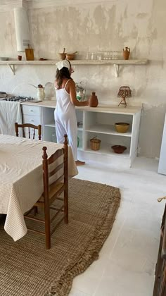 a woman standing in a kitchen next to a table with a white cloth on it