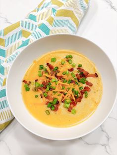 a white bowl filled with soup and topped with bacon, cheese and green onions next to a napkin